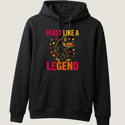 Bigfoot carrying a turkey with the text 'Feast Like A Legend' in colorful cartoon style. — printed on a unisex hoodie