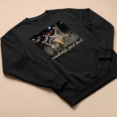 Photorealistic raccoon holding a coffee cup with the phrase 'somebody's feral Aunt' above it. — printed on a unisex sweatshirt