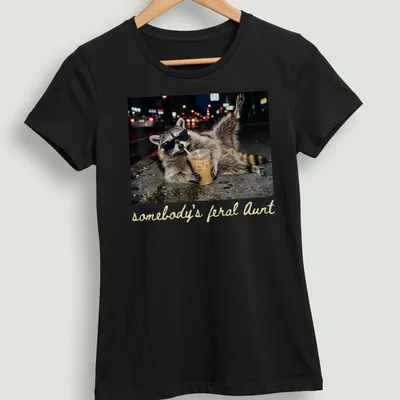 Photorealistic raccoon holding a coffee cup with the phrase 'somebody's feral Aunt' above it. — printed on a women's shirt