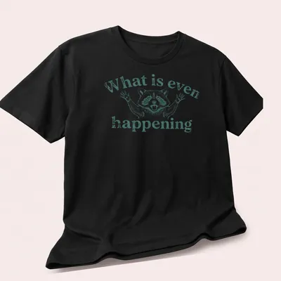 Vintage illustration of a puzzled raccoon with text 'What is even happening' — printed on a unisex t-shirt (angled view)