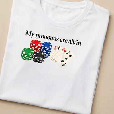 Graphic tee featuring poker chips and playing cards with bold text about pronouns — printed on a women's shirt
